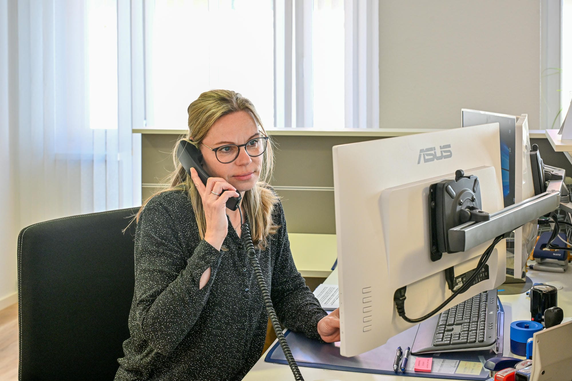 Eine Frau sitzt in einem hellen Büroraum an einem Computer und telefoniert.